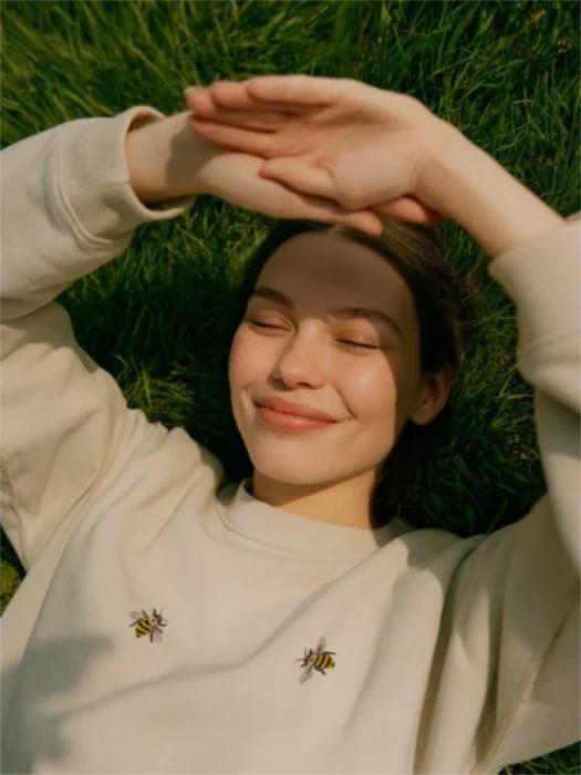 Cremefarbenes besticktes Sweatshirt mit zwei Bienen auf der Brust, getragen von Model auf einer Wiese im Sonnenlicht