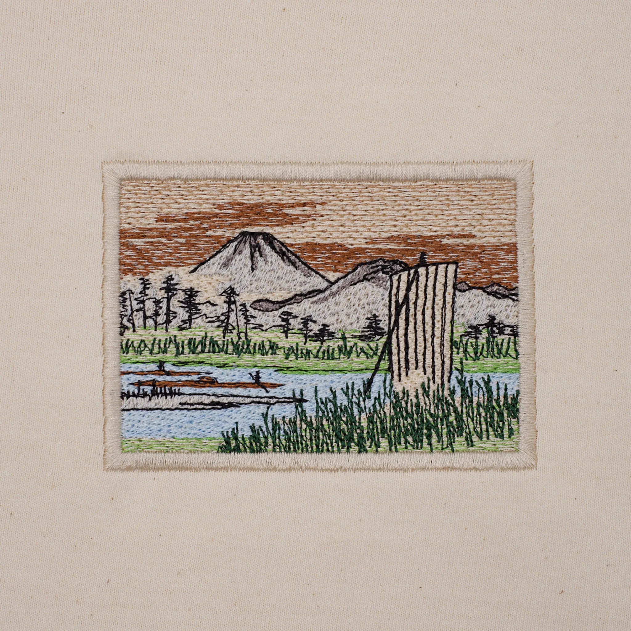 Close-up of machine embroidery: Mount Fuji, trees, river and reeds in satin and tatami stitches on cotton jersey