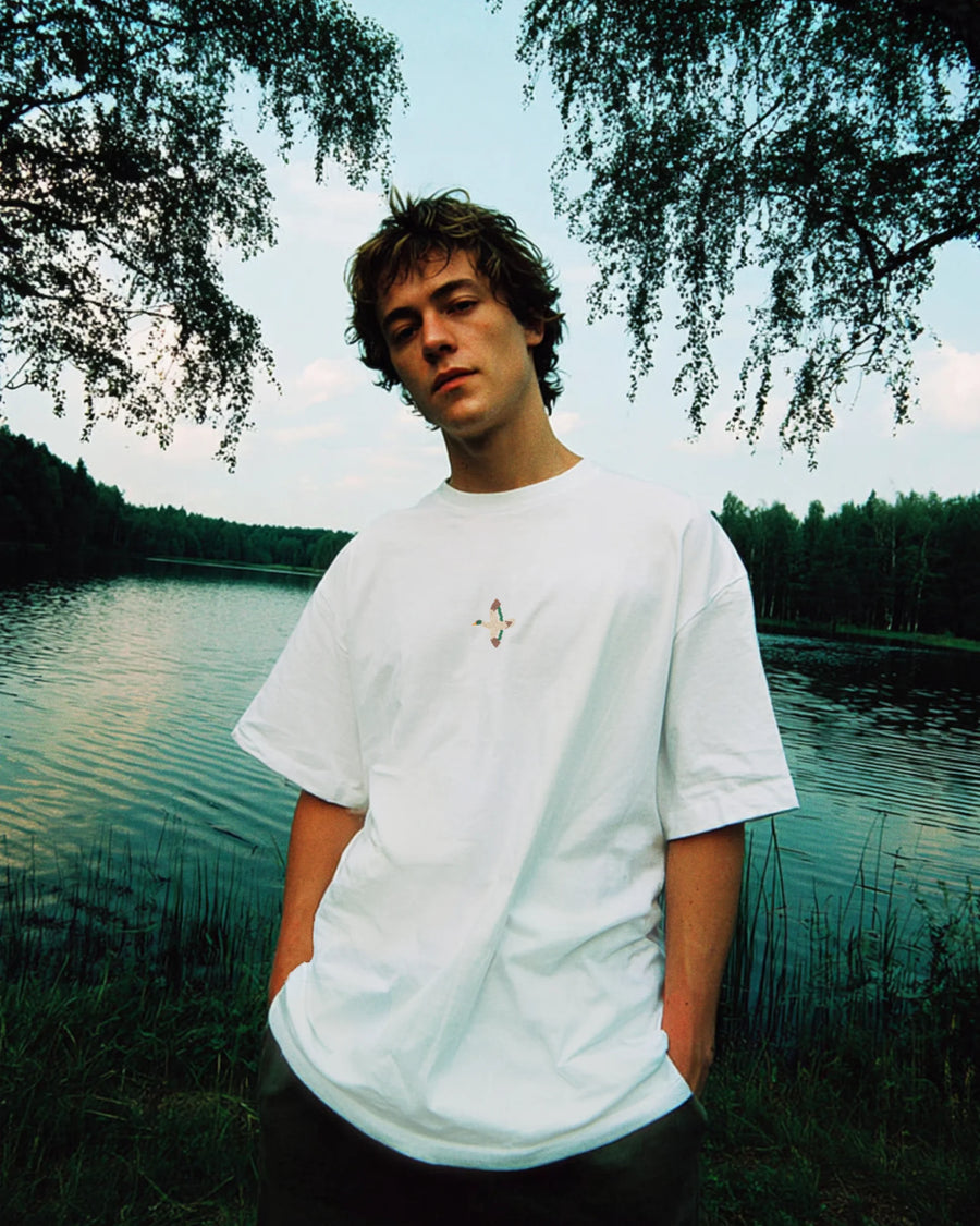Weißes besticktes T-Shirt mit kleiner Bruststickerei, getragen von Model am See in natürlicher Outdoor-Kulisse