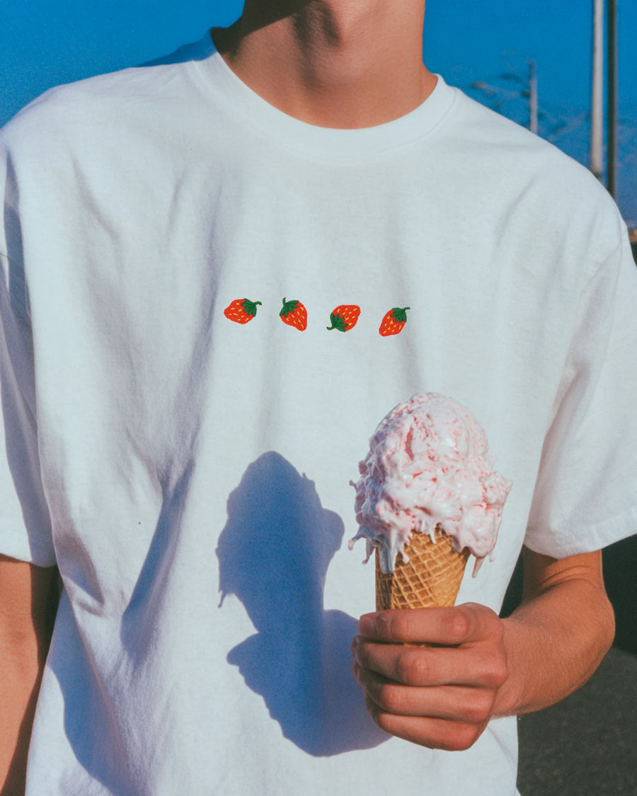 Weißes besticktes T-Shirt mit kleinen Erdbeeren auf der Brust, fotografiert mit Eiswaffel in sommerlicher Outdoor-Szene