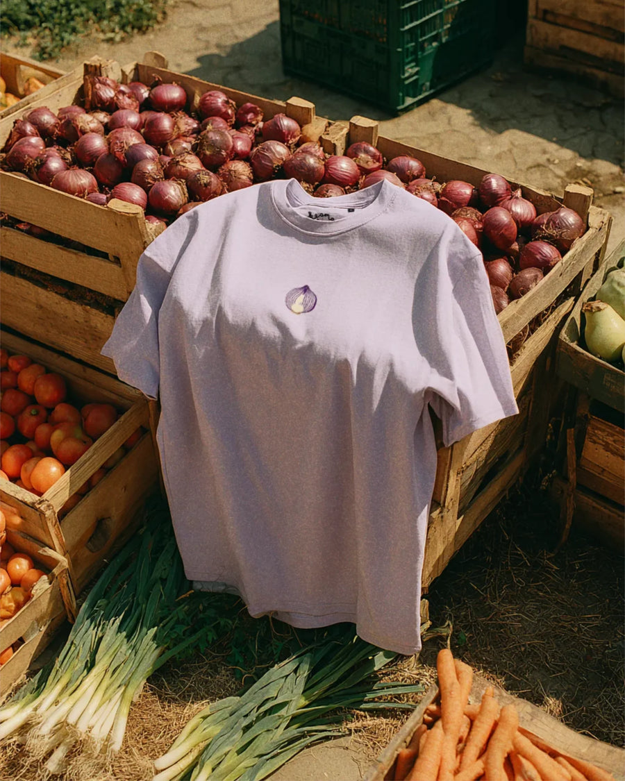 Helles besticktes T-Shirt mit kleiner Bruststickerei, inszeniert zwischen Gemüsekisten auf einem Markt im Freien